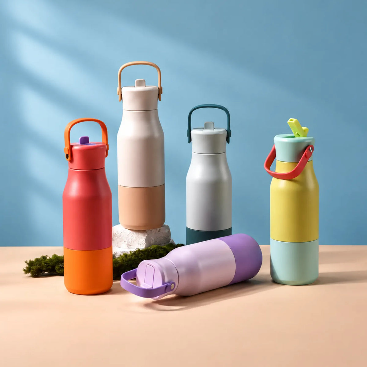 Five two-tone drink bottles grouped on a peach surface against a blue wall, one lying down.