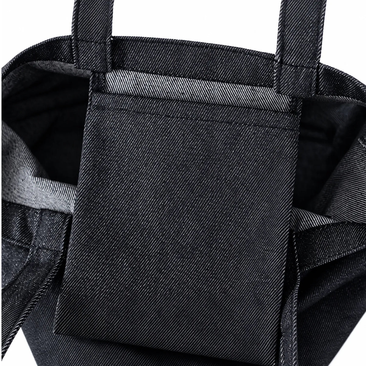 Close-up of a black denim tote bag showing a front slip pocket and the textured woven fabric of the main body.