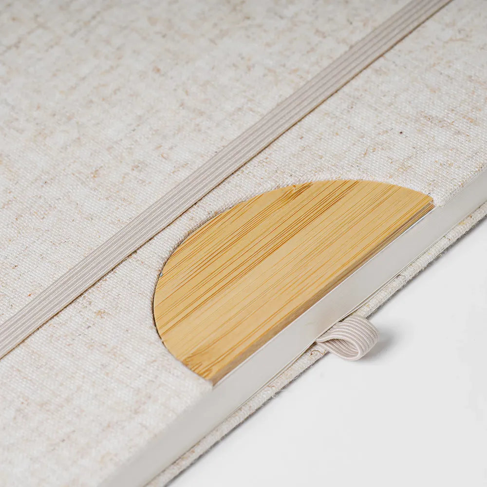 Close-up of A5 cotton linen notebook showing semi-circular bamboo bookmark integrated into elastic closure, natural textile cover texture visible