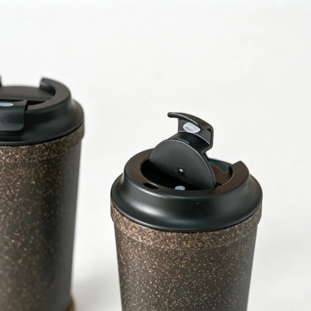 Close view of the black flip-top lid open on a dark brown recycled coffee grounds anti-tip travel cup, showing the sip opening, no branding applied