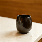 Dark brown aroma recycled coffee grounds coffee cup on a stone benchtop against a warm timber background, lifestyle setting, no branding applied