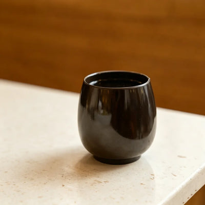 Dark brown aroma recycled coffee grounds coffee cup on a stone benchtop against a warm timber background, lifestyle setting, no branding applied