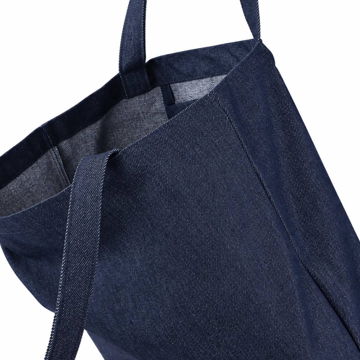 A close-up of a indigo denim tote bag with matching fabric handles, showing the textured weave and interior lining against a plain white background.
