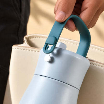 A hand lifting the teal loop handle away from a small post on a pale blue drink bottle lid.