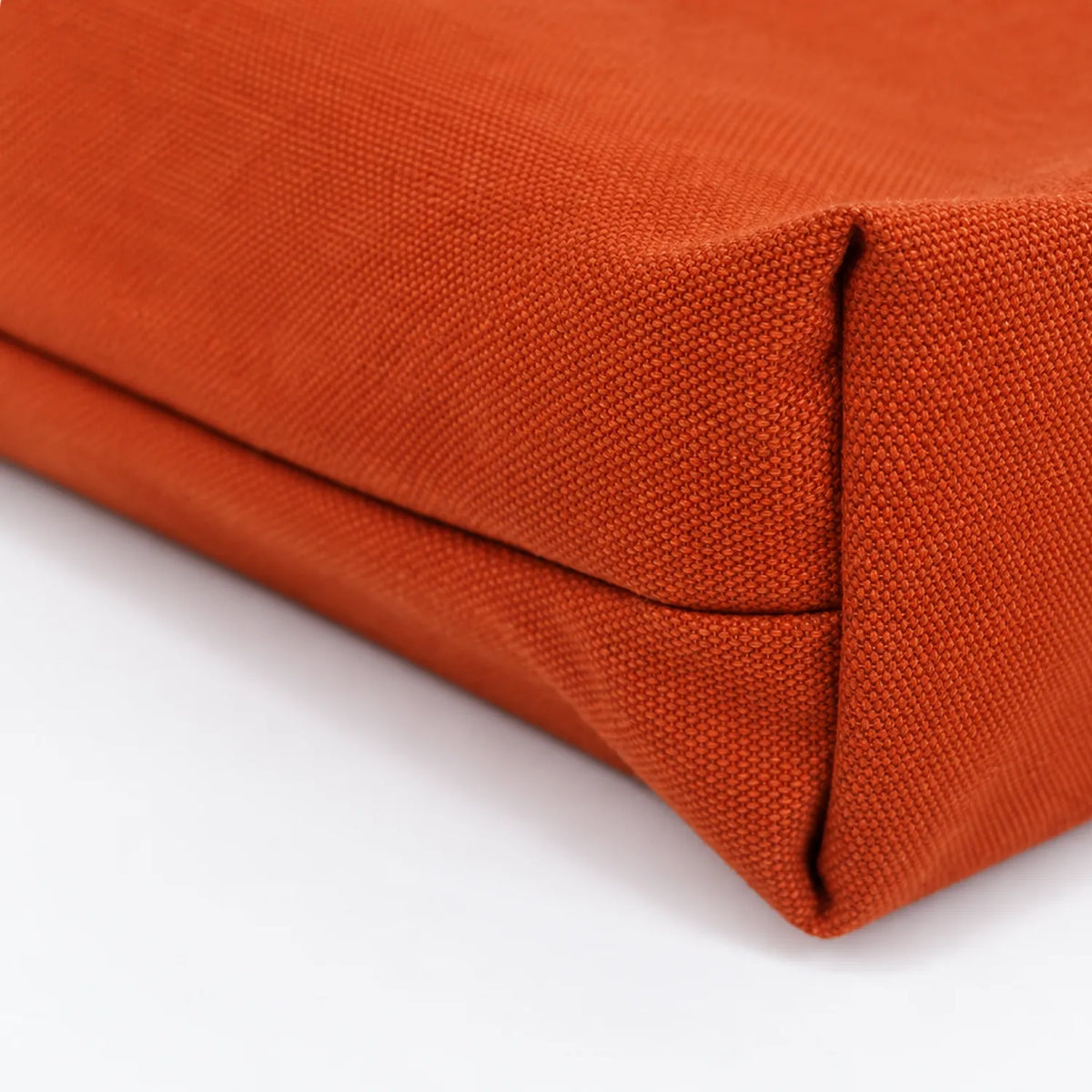 Close-up of a textured clay-orange woven canvas corner with a visible fold seam on a white background.