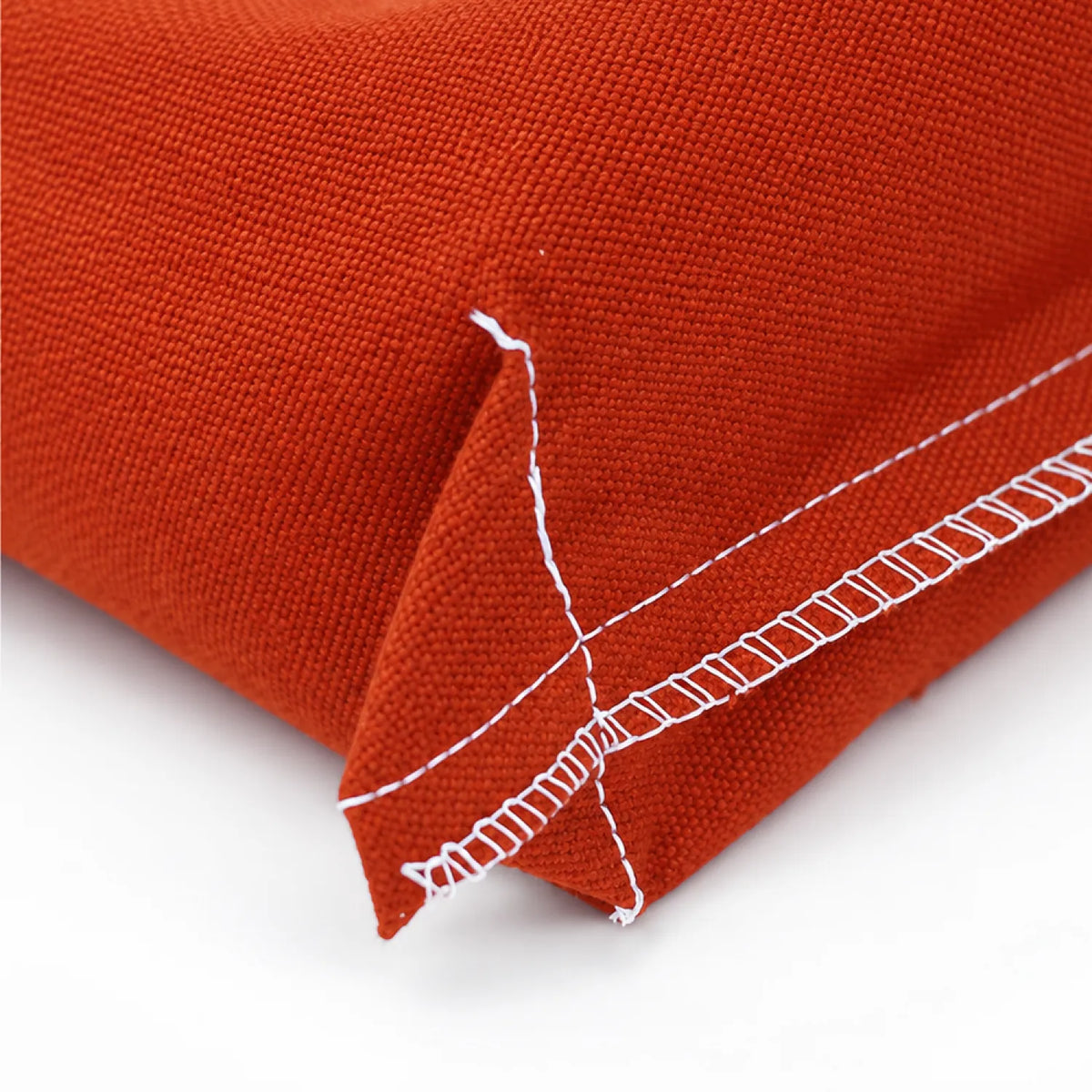 Close-up of a textured clay-orange woven canvas corner with white contrast stitching on a white background.