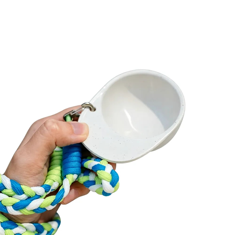 Hand holding an off-white hat-shaped recycled coffee grounds tasting cup by the brim with a blue and green braided lanyard, white background