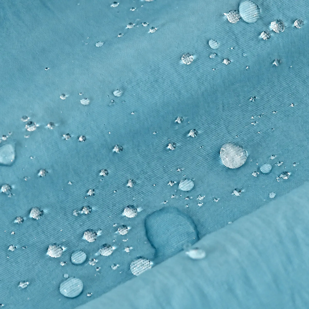 A close-up of a light blue water-repellent fabric surface with scattered water droplets beading on top.
