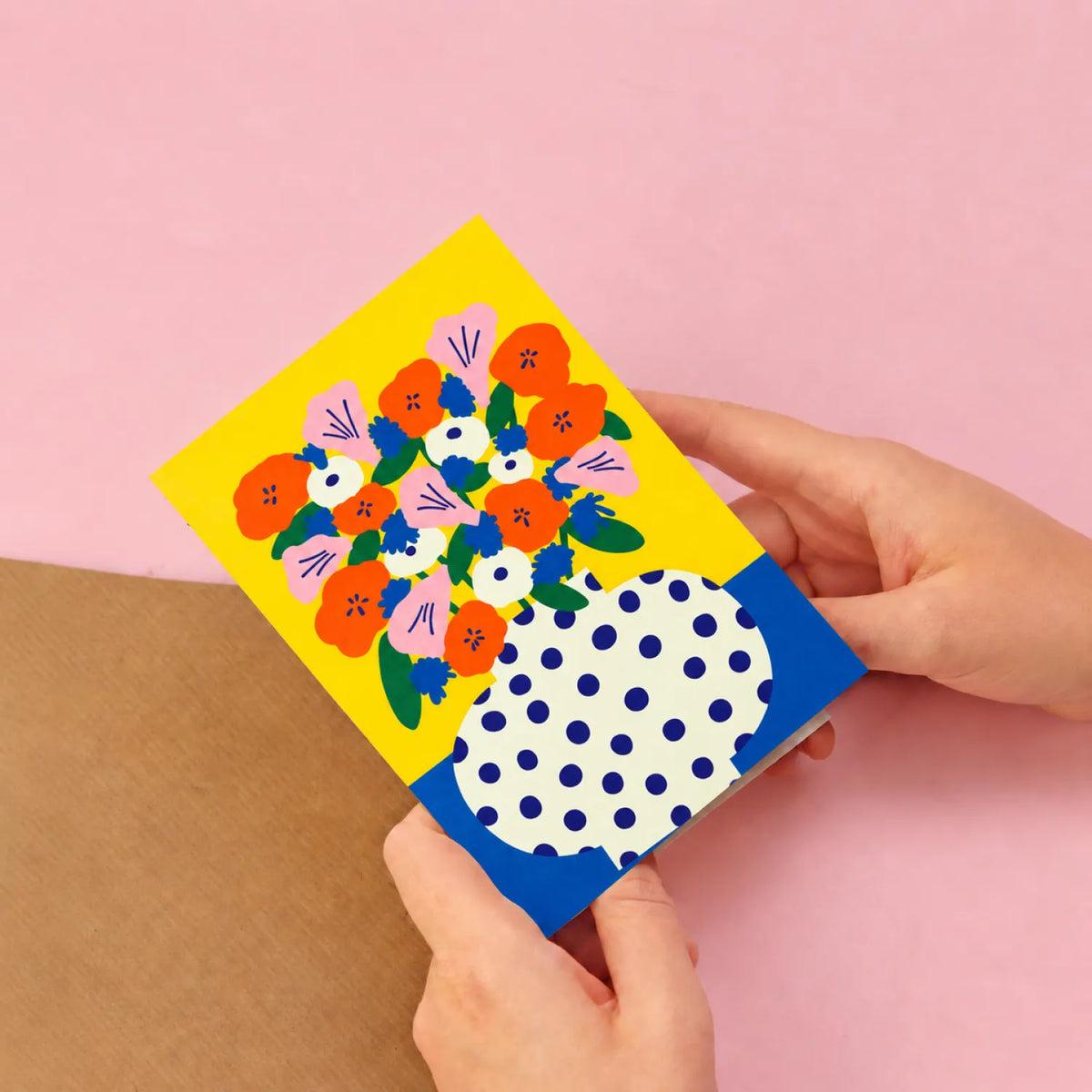 Hands holding the Sunny Blooms illustrated greeting card, showing its size against a pink wall