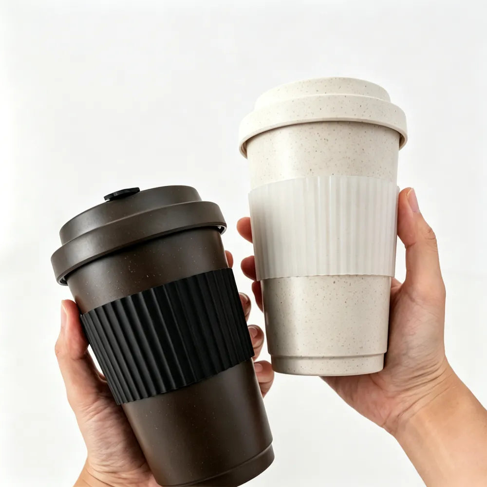 Two hands holding off-white and dark brown recycled coffee grounds travel cups side by side against a white background, showing the silicone grip bands and lids, no branding applied