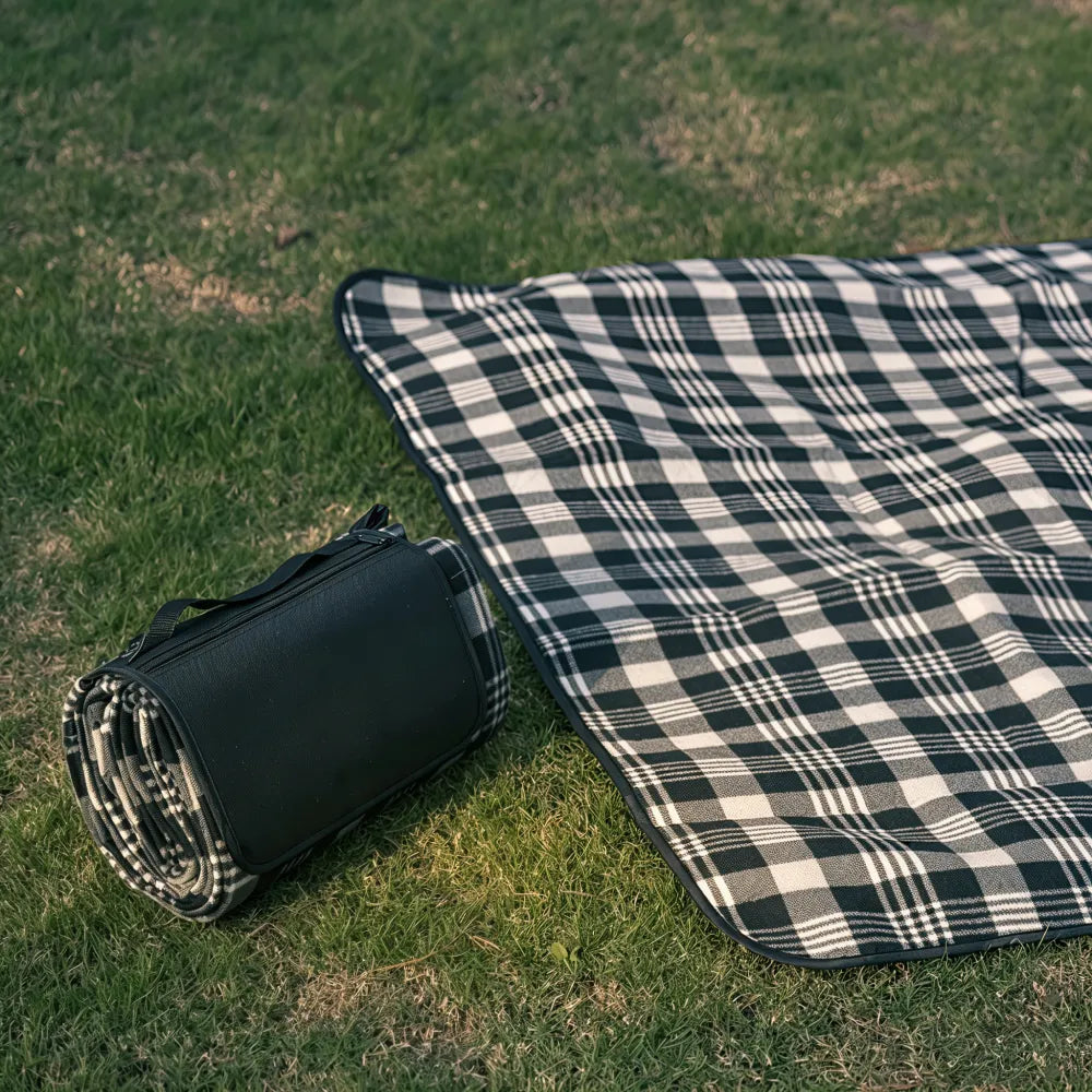 Black and white check picnic mat partly unrolled on grass beside its folded carry case, showing the fleece top, no Wumble branding applied