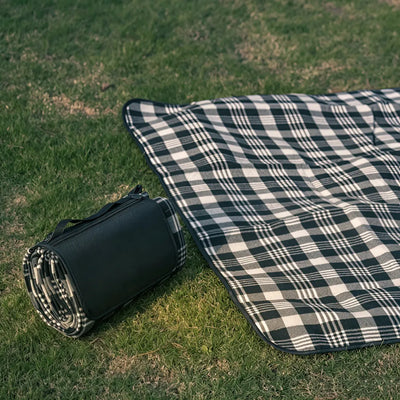 Black and white check picnic mat partly unrolled on grass beside its folded carry case, showing the fleece top, no Wumble branding applied