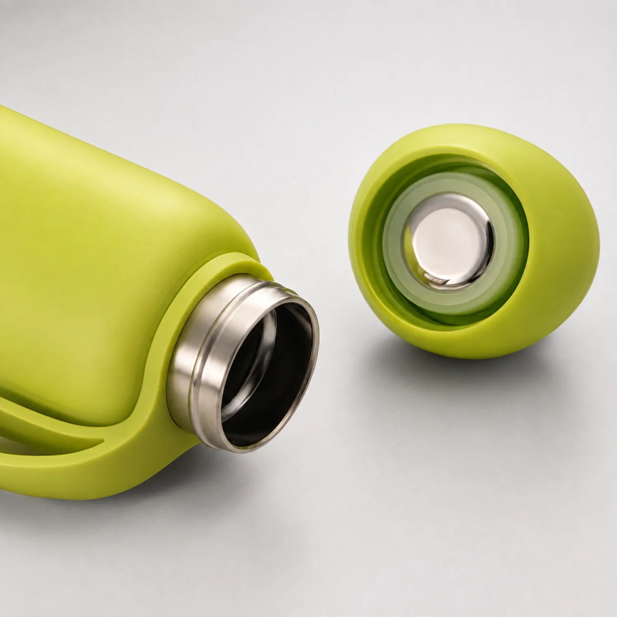 Yellow-green drink bottle on its side with the cap off, showing a polished neck and a silver disc in the cap.