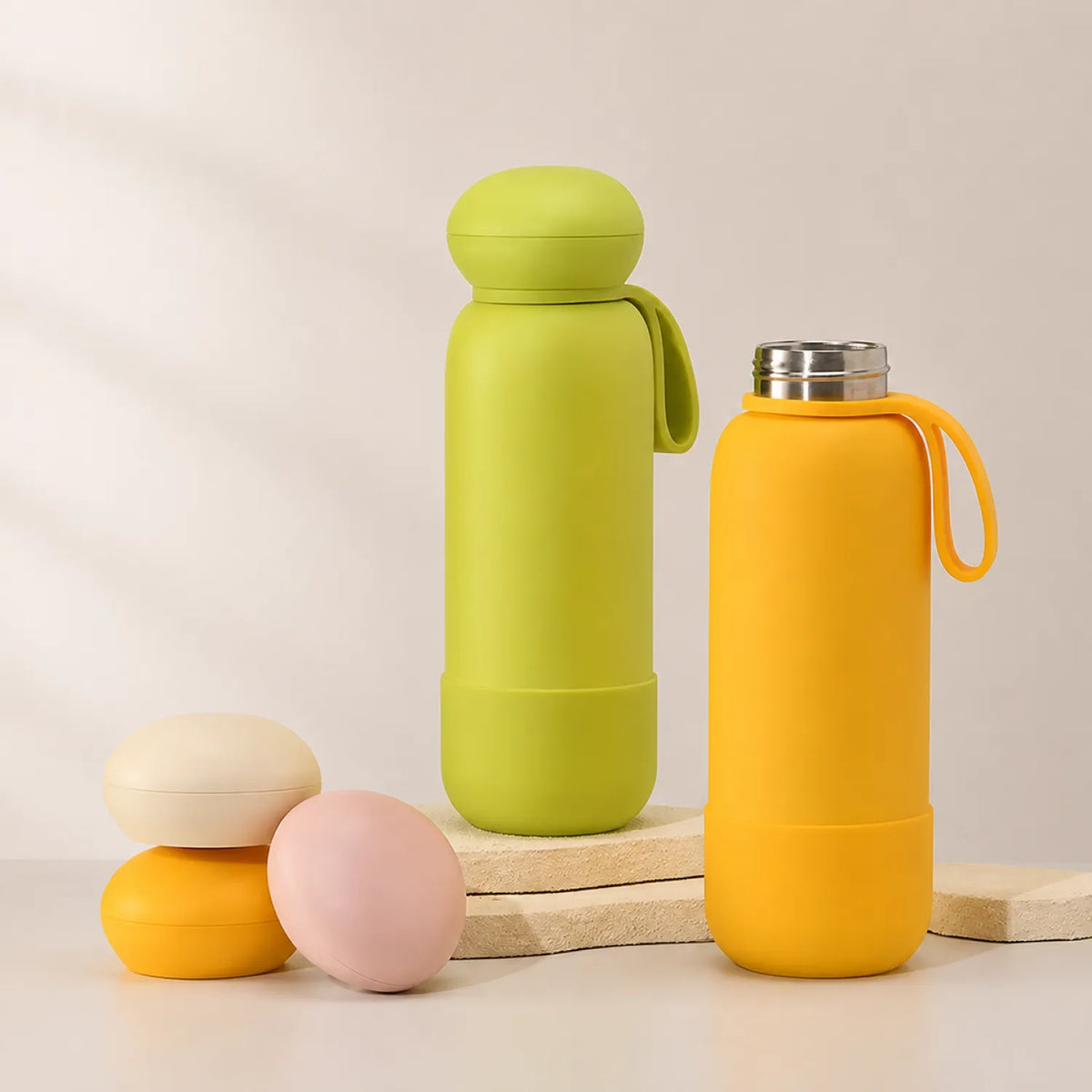 Two drink bottles, green and orange, styled with three loose caps on stone slabs against a cream backdrop.