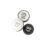 Round recycled coffee grounds coasters printed with a sample "good coffee goes here" design and smiley motif in off-white and dark brown beside a branded tin, white background, branded example