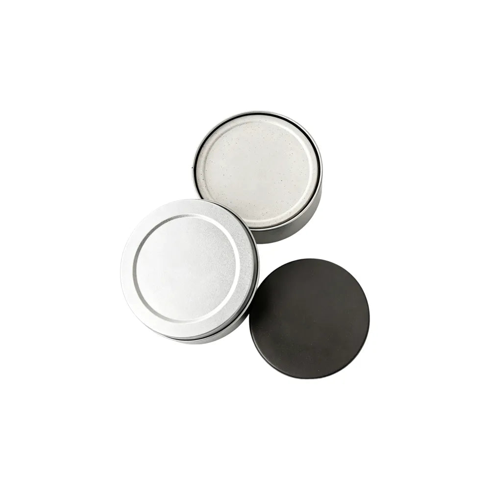 Open round metal tin holding off-white recycled coffee grounds coasters beside its lid, showing the gift tin packaging, no branding applied