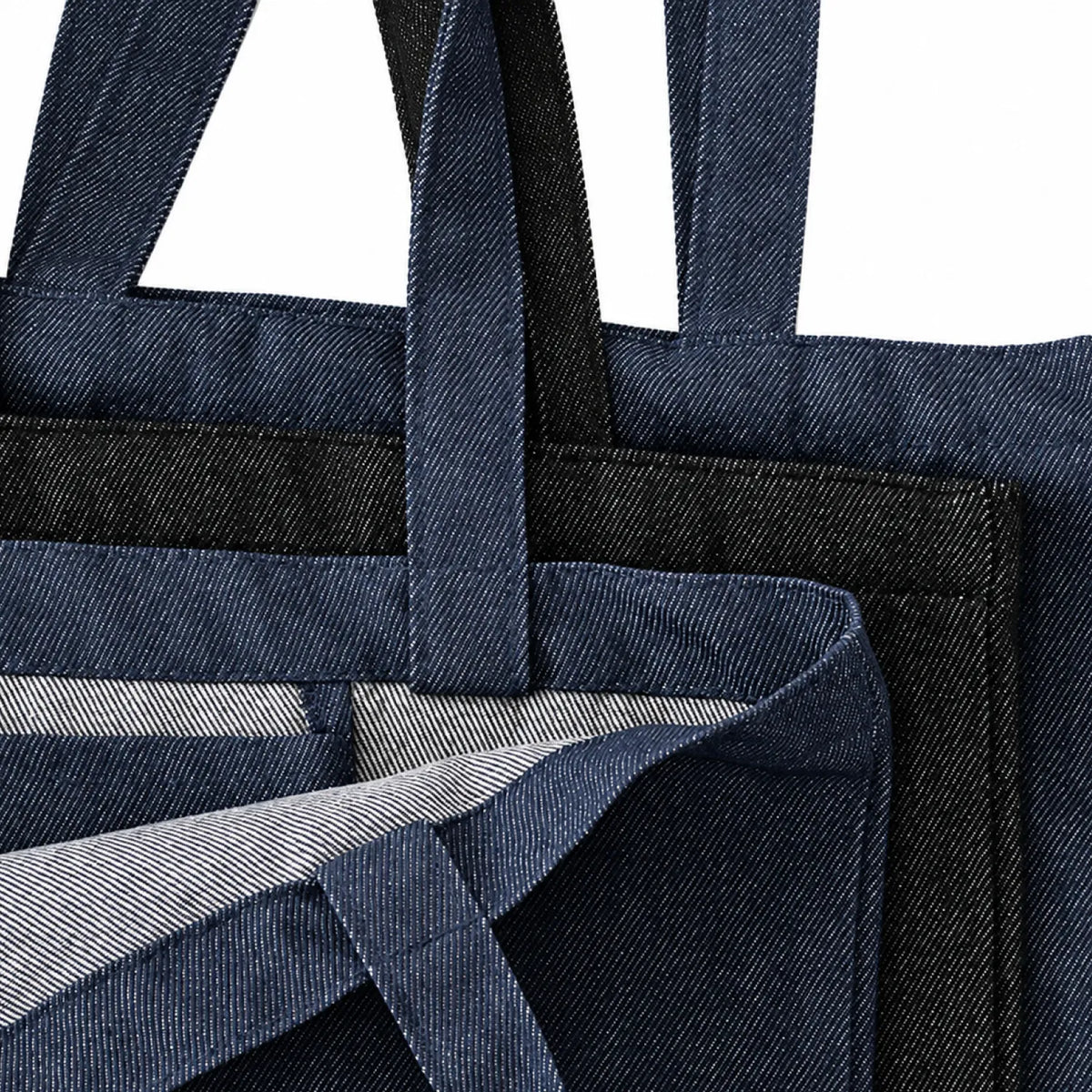 Close-up of denim tote bags with handles and a striped interior lining in black and indigo blue, shown against a white background.