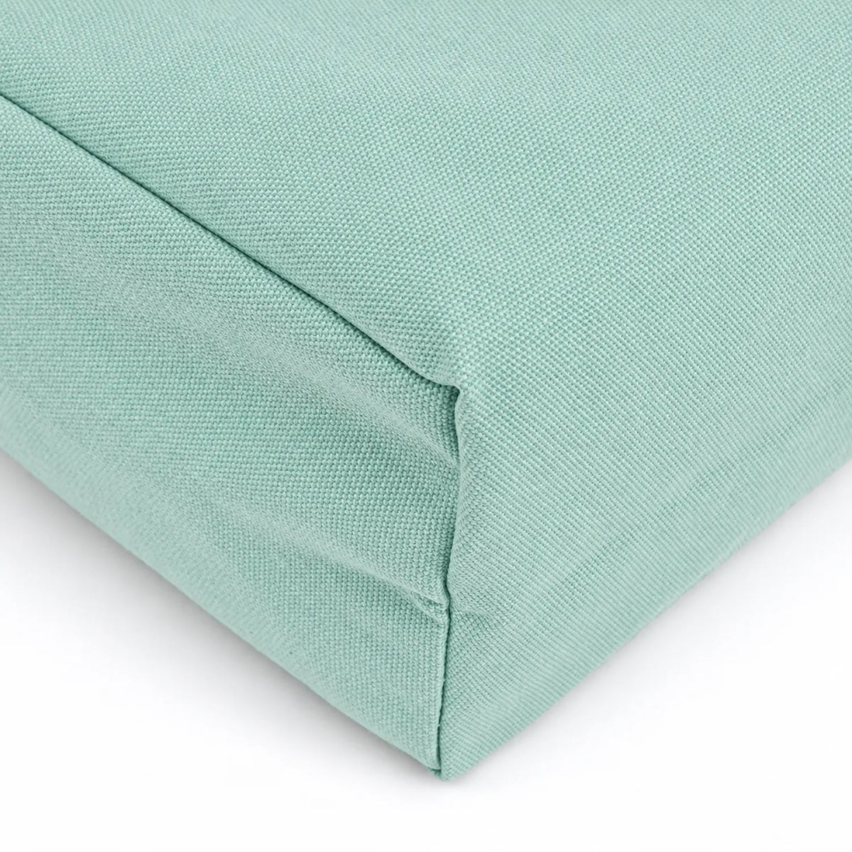 A close-up of a soft teal green fabric cushion corner showing the woven texture and stitched seam against a white background.