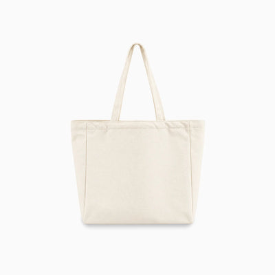 A plain canvas tote bag in a light cream or off-white color, featuring two long shoulder straps and a structured rectangular shape, shown against a solid white background.